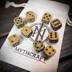Könnte beinhalten: Neun beige Würfel mit schwarzen Augen liegen um einen Stoffbeutel. Auf dem Beutel sind ein Logo und das Wort "MYTHCRAFT" aufgedruckt. Die Würfel sind für Spiele gedacht. Der Beutel ist aus naturfarbenem Stoff.