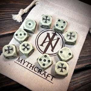 May include: A set of ten dice with a weathered, stone-like appearance. Each die features black markings, including a cross symbol on some faces. The dice are displayed on a beige fabric bag with the text "MYTHCRAFT" and a logo.