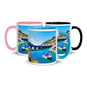 May include: Three white ceramic mugs with colorful interiors and handles. Each mug features a scenic image of a bridge over a blue body of water with boats. One mug has a pink interior and handle, another has a blue interior and handle, and the third has a black interior and handle.