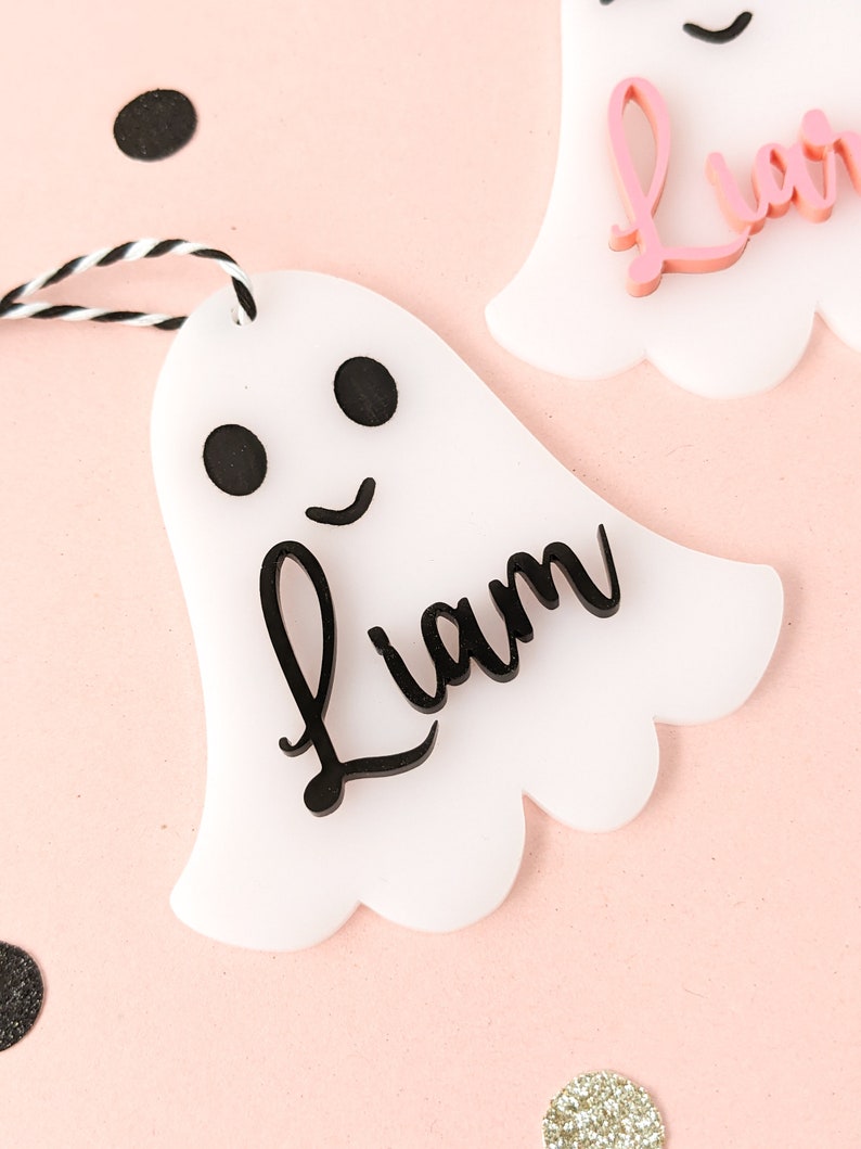 May include: White ghost-shaped ornament with a black outline and black eyes. The ornament has the name "Liam" written in black cursive lettering.
