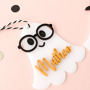 May include: White ghost-shaped gift tag with black glasses and a smiling face. The name "Mathew" is written in orange on the tag.