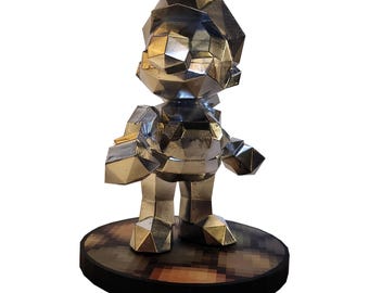 May include: A silver-colored geometric sculpture of a character, standing on a round base with a pixelated design. The figure has a polygonal design, with a hat and overall shape reminiscent of a video game character.