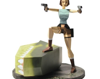 May include: A papercraft figurine of a woman in a light blue top and brown shorts, holding two silver pistols. She stands on a geometric green and gray structure, with a black base. The figure has brown hair and boots.