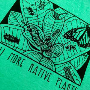 May include: A light green t-shirt featuring a black and white illustration of insects, caterpillars, and a butterfly on leaves. The text "GROW MORE NATIVE PLANTS" is printed in black. The design is enclosed in a black square.