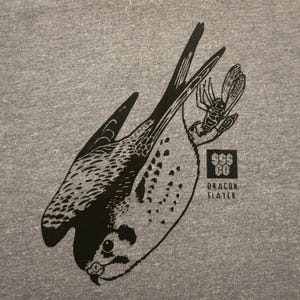 May include: A gray t-shirt featuring a black and white illustration of a falcon holding an insect. The design includes the text "SSS CO" and "DRAGON SLAYER" in a square logo.
