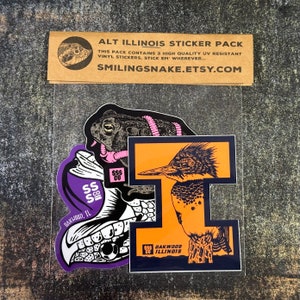 May include: A sticker pack featuring three illustrated designs: a frog with a pink worm, a kingfisher bird, and a skull with the text "Oakwood, IL". The stickers are on a clear plastic background.