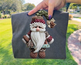 May include: A handcrafted Santa Claus ornament with a white beard, red and white hat, and brown and white patterned sleeves. The ornament has a pink nose and is held against a gray background.
