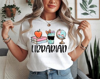 May include: White t-shirt with a colorful graphic design featuring an apple, books, a coffee cup, and a globe. The word "LIBRARIAN" is printed in bold, black letters below the illustrations. The shirt is a casual style.