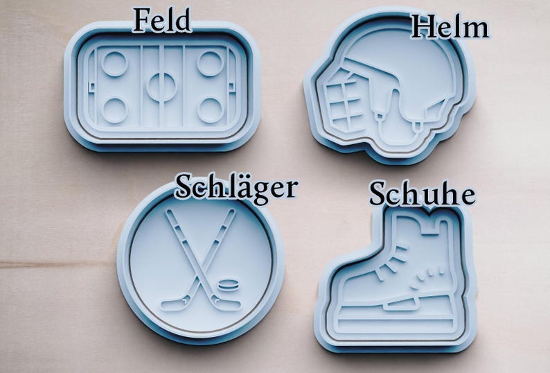 May include: Four blue plastic cookie cutters shaped like hockey equipment. The cutters are labeled "Feld", "Helm", "Schl&auml;ger", and "Schuhe".