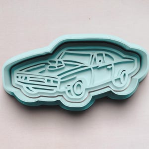 May include: A light blue plastic cookie cutter shaped like a classic muscle car. The car has a detailed design with a hood scoop and wheels.