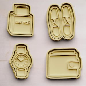 Könnte beinhalten: Vier Ausstecher in Form einer Parfümflasche, eines Schuhpaares, einer Uhr und einer Brieftasche. Die Ausstecher sind aus hellgelbem Kunststoff.