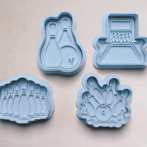 Puede incluir: Conjunto de cuatro cortadores de galletas de plástico azul con forma de bolos y una bola de bolos. Los cortadores están diseñados para crear galletas con forma de bolos y una bola de bolos.