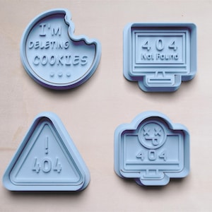 Könnte beinhalten: Vier blaue Ausstecher mit verschiedenen Designs. Ein Ausstecher ist in Form eines Kekses mit dem Text "I'm deleting cookies". Ein weiterer Ausstecher ist in Form eines Computerbildschirms mit dem Text "404 Not Found". Der dritte Ausstecher ist in Form eines Dreiecks mit dem Text "! 404". Der vierte Ausstecher ist in Form eines Computerbildschirms mit einem Gesicht und dem Text "404".