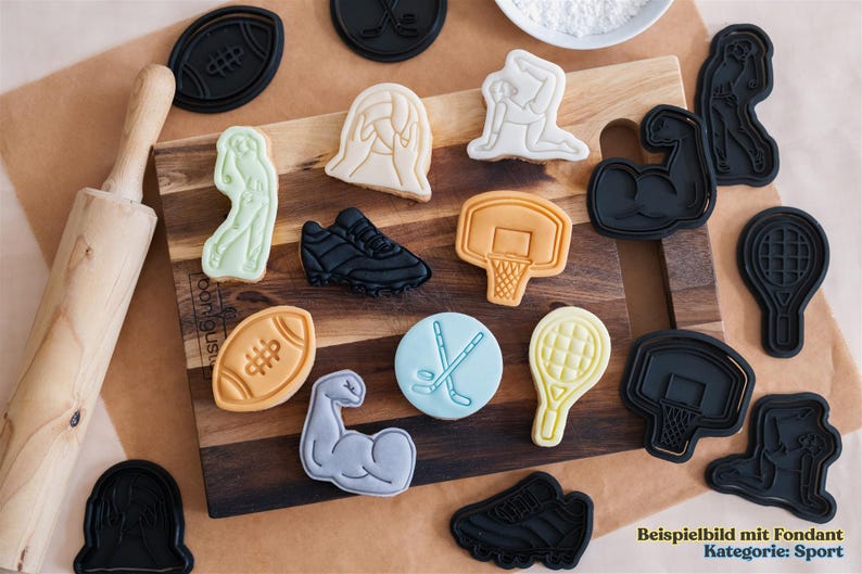 May include: A collection of black and white cookie cutters shaped like various sports equipment, including a football, basketball, tennis racket, hockey stick, and a weightlifting arm. The cookie cutters are arranged on a wooden surface with a rolling pin and several cookies decorated with fondant.
