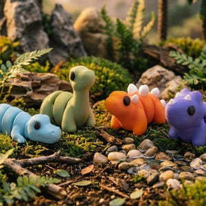 May include: Four small dinosaur figurines in light blue, sage green, orange, and purple. Each creature features a smooth, segmented body, a rounded head with black circular eyes, and a distinct posture. The orange and purple figures have small spikes.