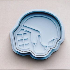 May include: A light blue plastic cookie cutter shaped like a hockey helmet.