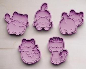 Puede incluir: Cinco cortadores de galletas morados con forma de gato en varias poses. Los cortadores presentan contornos detallados de gatos en diferentes posiciones, incluyendo sentados, estirándose y saludando. Estas herramientas están diseñadas para crear galletas o pasteles con temática de gatos.