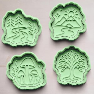 Puede incluir: Cuatro cortadores de galletas verde claro con diseños temáticos de la naturaleza. Los diseños incluyen una escena de río con árboles, una escena de montaña con un sol, setas y un árbol con hojas. Los cortadores son de plástico.