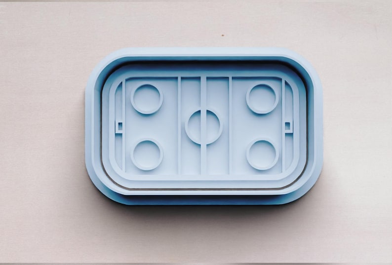 May include: A light blue plastic cookie cutter shaped like a hockey rink with four circles for cookies and a center circle.