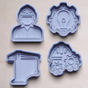 Könnte beinhalten: Vier violette Plastik-Ausstecher in Form eines Bauarbeiters, einer Glühbirne in einem Zahnrad, eines Bauhelms mit einem Zahnrad und eines Gebäudes mit einem Balken.
