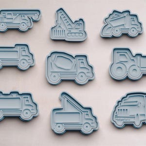 May include: Nine blue plastic cookie cutters shaped like different construction vehicles. The cutters include a cement mixer, a tipper truck, a crane, an articulated lorry, a bulldozer, and a pick-up truck.