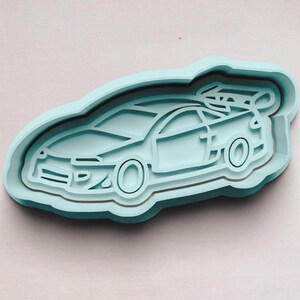 May include: A light blue plastic cookie cutter shaped like a car. The car has a detailed design with a front grill, headlights, and wheels.