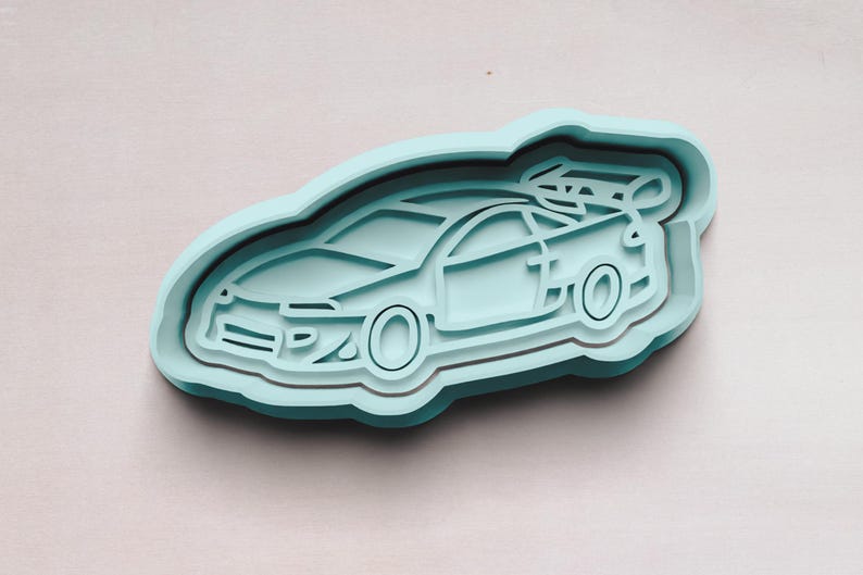May include: A light blue plastic cookie cutter shaped like a car. The car has a detailed design with a front grill, headlights, and wheels.