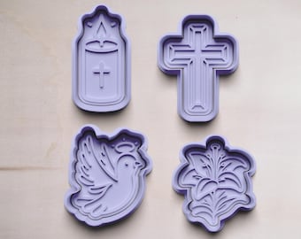 Könnte beinhalten: Vier violette Plastik-Ausstecher in Form einer Taube, eines Kreuzes, einer Kerze und einer Lilie. Die Ausstecher liegen auf einer hellbraunen Holzoberfläche.