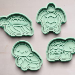 May include: Four green plastic turtle cookie cutters. The cutters are in the shape of turtles with different designs.