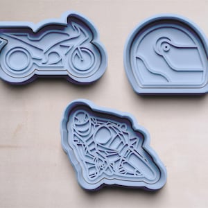 Könnte beinhalten: Drei blaue Plastik-Ausstecher in Form eines Motorrads, eines Helms und einer Person, die ein Motorrad fährt.