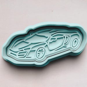 May include: A light blue plastic cookie cutter shaped like a sports car. The car is facing to the right and has a detailed design.