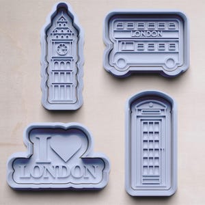 May include: Four gray plastic cookie cutters shaped like London landmarks: Big Ben, a double-decker bus, a telephone booth, and a heart with "I love London" written on it.