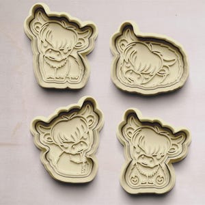 May include: Four cookie cutters shaped like Highland cows, each with a different pose. The cutters are made of a beige plastic material.