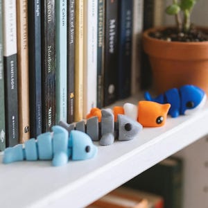 May include: Three articulated plastic animal figures in light blue, gray, and orange and white. The light blue figure is shaped like a dolphin, the gray figure resembles a shark, and the orange and white figure features a cat-like design.
