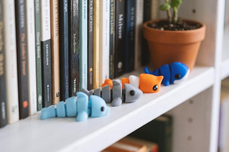 May include: Three articulated plastic animal figures in light blue, gray, and orange and white. The light blue figure is shaped like a dolphin, the gray figure resembles a shark, and the orange and white figure features a cat-like design.