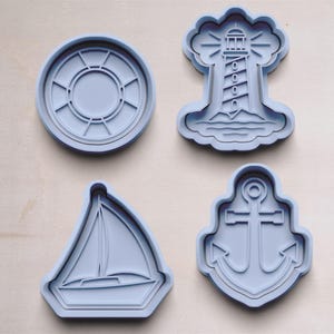 May include: Four blue plastic cookie cutters shaped like a lighthouse, an anchor, a sailboat, and a life preserver.