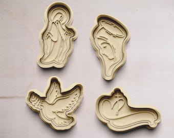 May include: Four cookie cutters made of beige plastic. The cutters are shaped like a dove, a woman with a halo, a woman with a halo and a heart, and a heart with a cross.