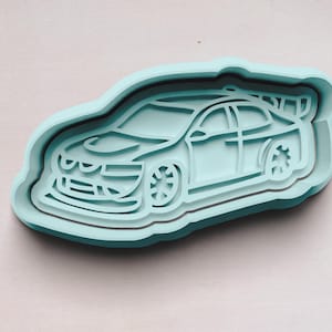May include: A light blue plastic cookie cutter shaped like a race car. The car has a black outline and a detailed design.