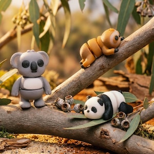 May include: Three small animal figurines made of smooth material: a standing grey koala with a white belly, a climbing tan sloth with dark eye patches, and a resting black and white panda, all positioned on a textured wooden branch with green leaves.