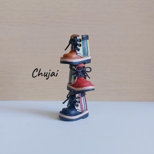 May include: Three miniature boots stacked on top of each other. The top boot is brown with a black top and striped accents. The middle boot is red, and the bottom boot is navy blue with striped accents. The text "Chujai" is in the image.