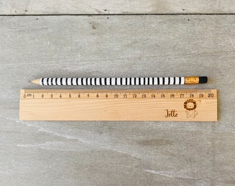 May include: A wooden ruler with black and white stripes, a lion illustration, and the name "Jette" engraved on it. The ruler measures 20 centimetres.