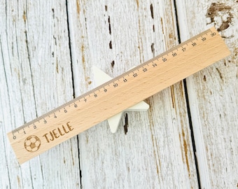 May include: A wooden ruler with a football design and the name "TJELLE" engraved on it. The ruler is 50.8 cm long and has markings for each centimetre.
