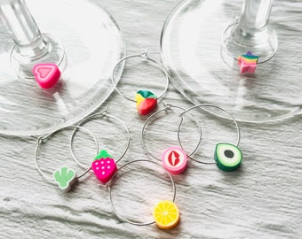 May include: Set of six colorful wine glass charms featuring a variety of fruit and heart designs. The charms are attached to silver rings.
