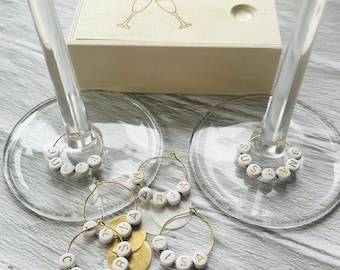 May include: Five gold-colored wine glass charms with white beads spelling out the names "Julia", "Maria", "Suzanne", "Cherrysa", and "Lisa".