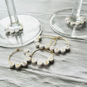May include: Four gold-toned wine glass charms with white beads spelling out the names "Chelsea", "Lisa", "Jana", and "Maria".