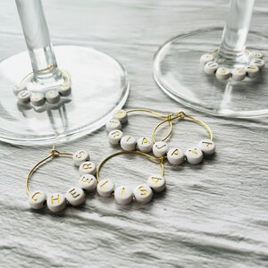 May include: Four gold-toned wine glass charms with white beads spelling out the names "Chelsea", "Lisa", "Jana", and "Maria".