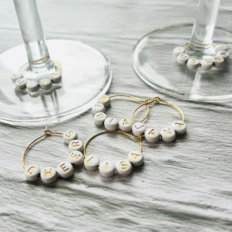 May include: Four gold-toned wine glass charms with white beads spelling out the names "Chelsea", "Lisa", "Jana", and "Maria".