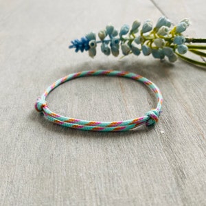 Könnte beinhalten: Ein türkisfarbenes und rosafarbenes Armband mit Muster und einem geknoteten Verschluss.