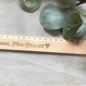 K&ouml;nnte beinhalten: Ein Holzlineal mit einem schwarzen Herz und dem eingravierten Text "DANKE, FRAU M&Uuml;LLER".