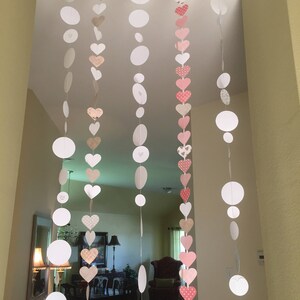 Puede incluir: Círculos de papel blanco y corazones con estampado rosa y beige enhebrados para crear una guirnalda para una fiesta o un evento especial.